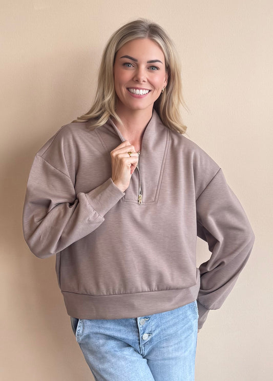 Woman wearing a brown pullover with a zipper against a beige background