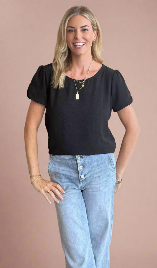 Woman wearing a black top and light blue jeans against a beige background