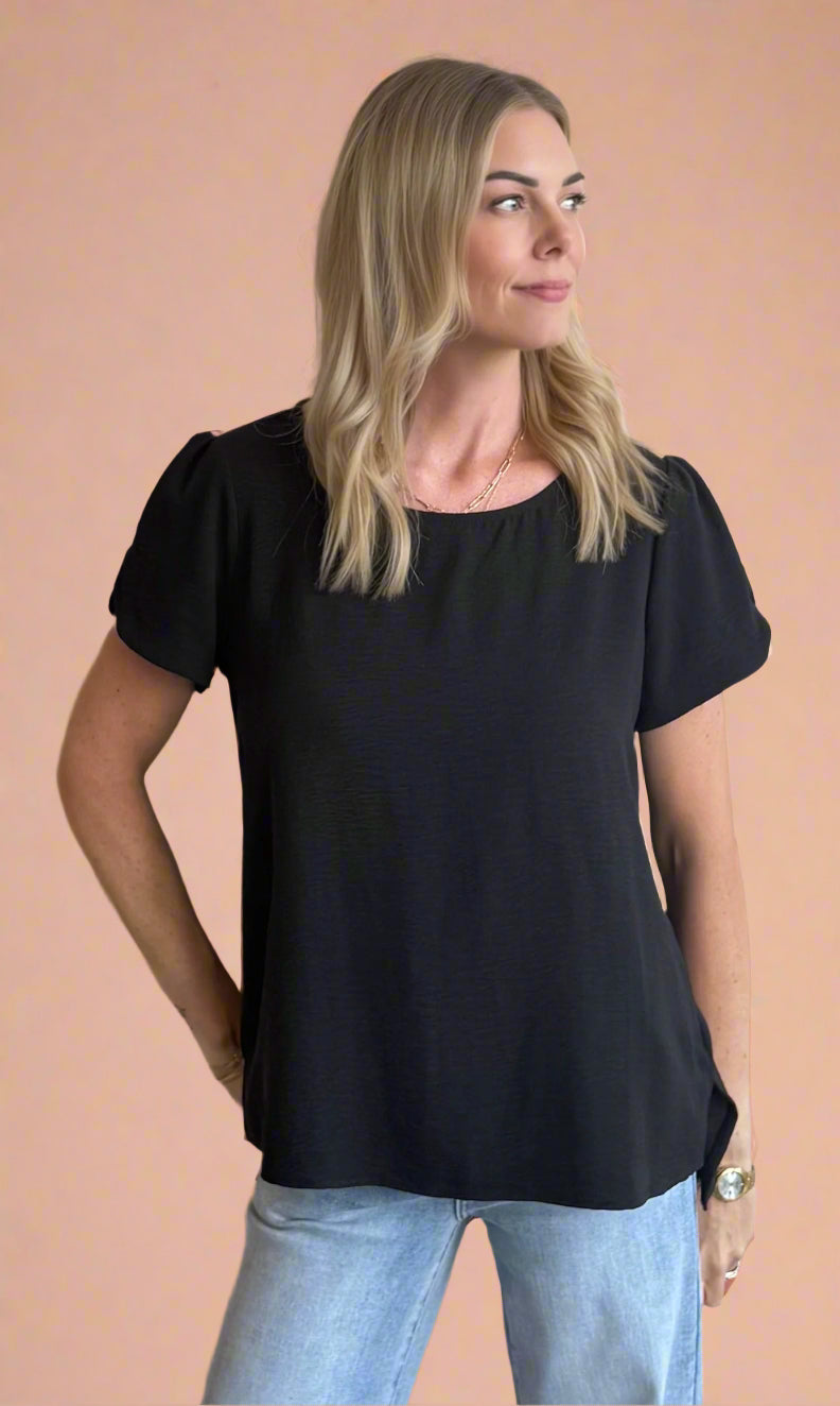 Woman wearing a black top and light blue jeans against a beige wall