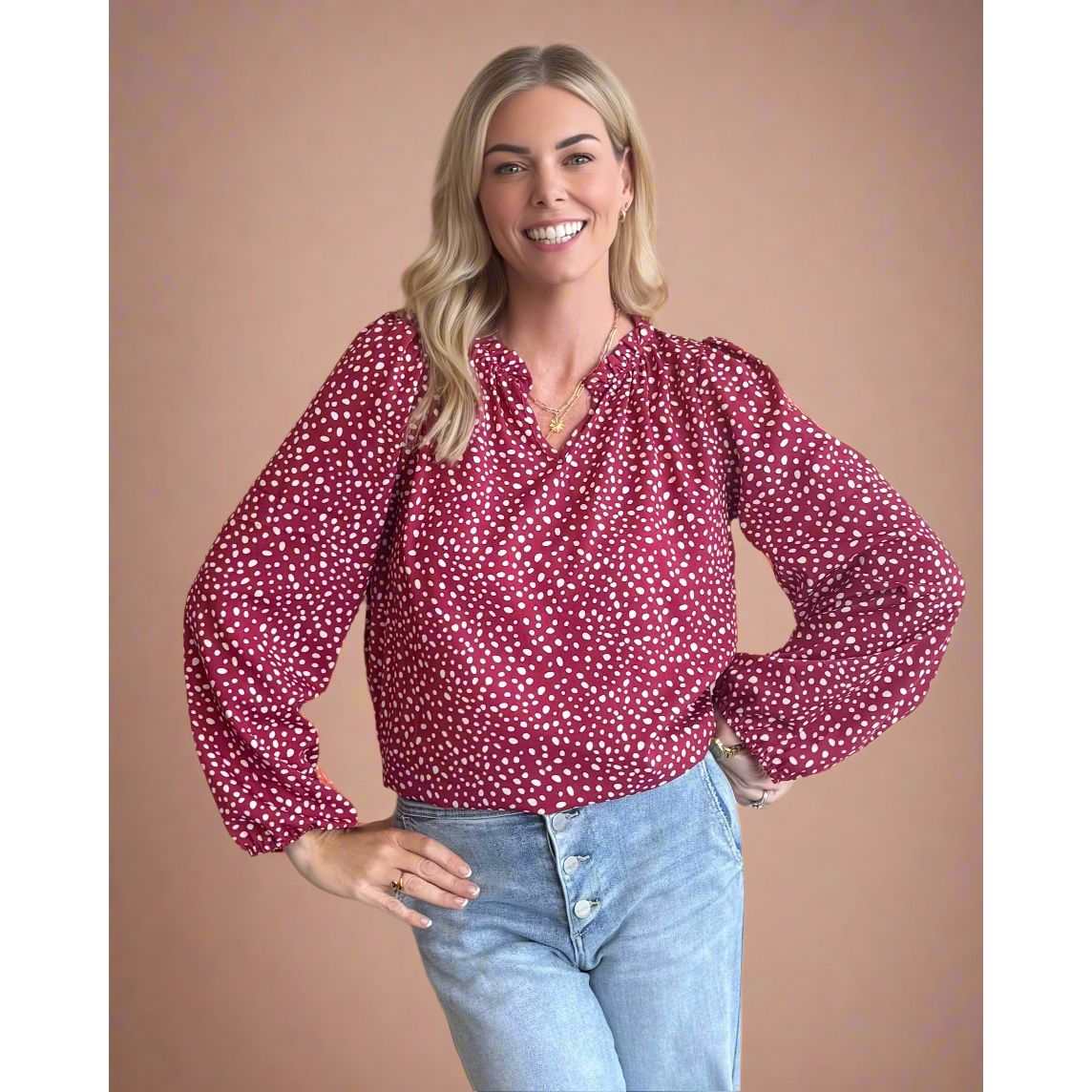 Woman wearing a red polka dot blouse and blue jeans against a beige background