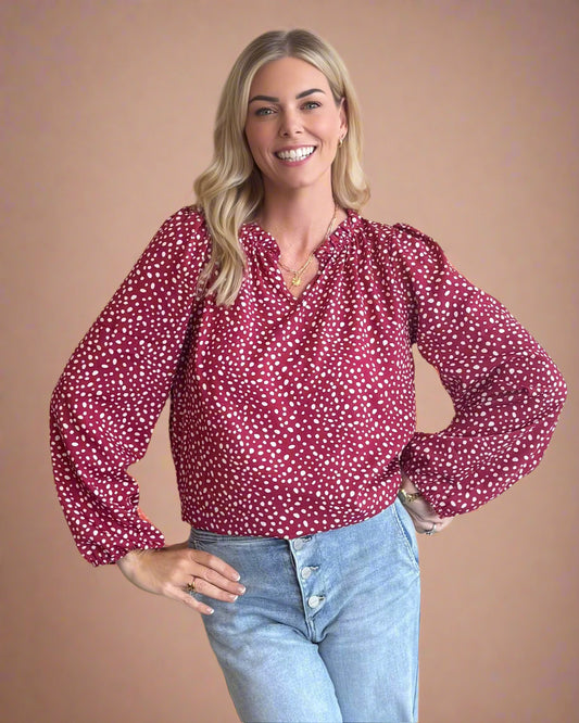 Woman wearing a red polka dot blouse and blue jeans against a beige background