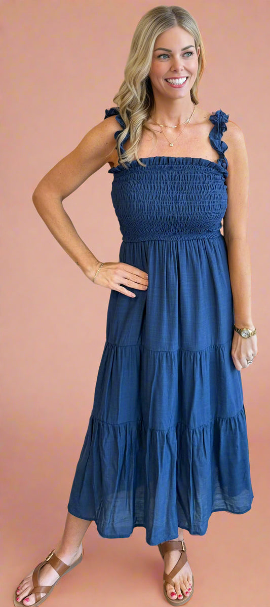 Woman wearing a blue dress with ruffled straps against a beige wall.
