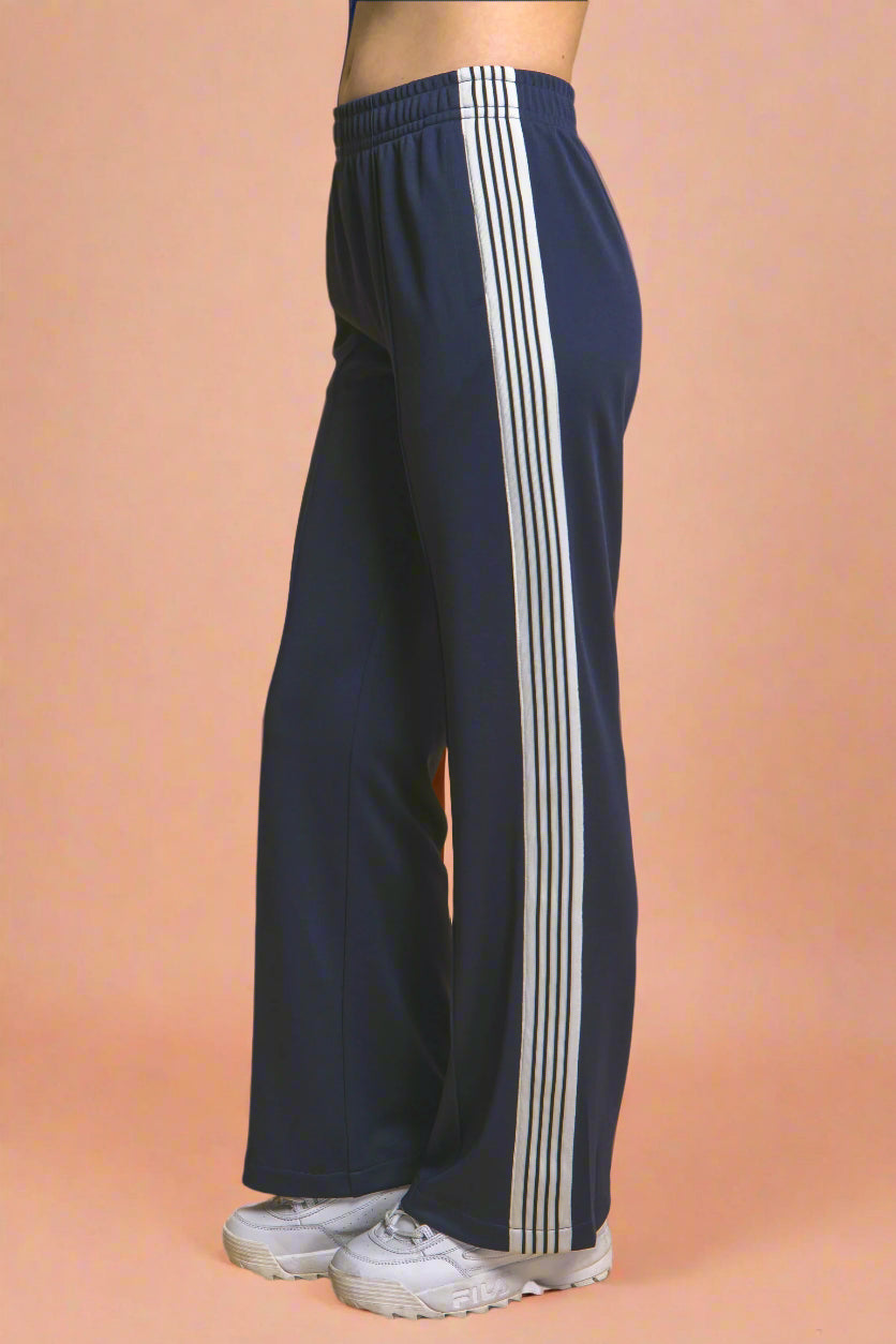 Navy blue track pants with white stripes on a mustard yellow background