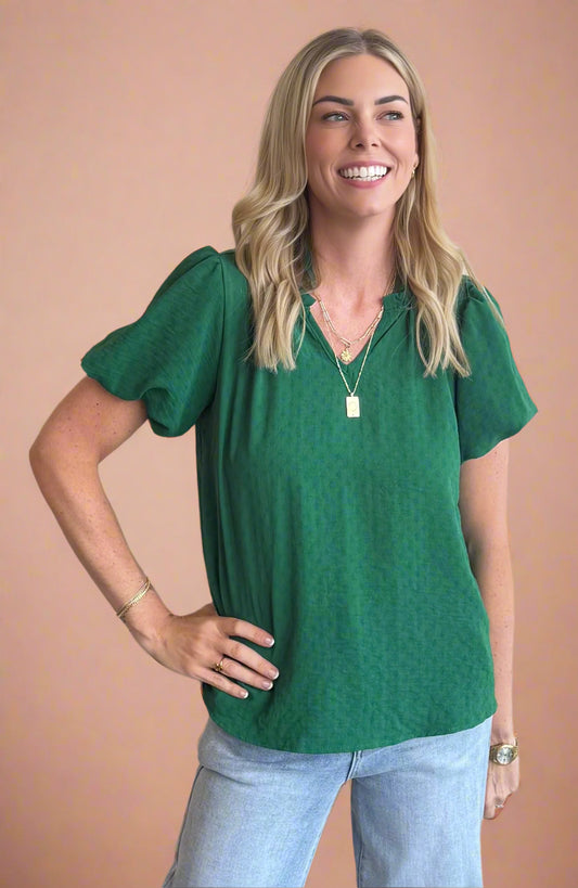Woman wearing a green blouse and light blue jeans against a beige background