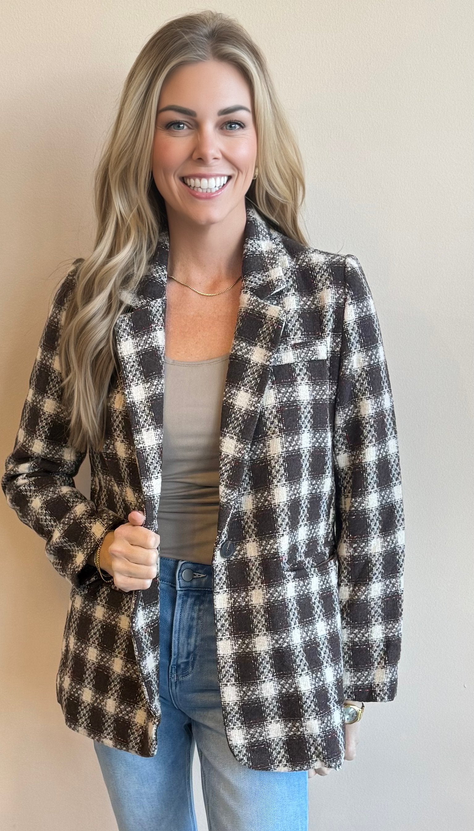 Woman wearing a chocolate brown checkered blazer against a plain background 