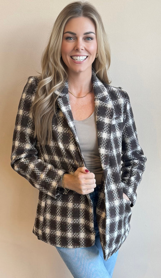 Woman wearing a chocolate brown checkered blazer against a plain background