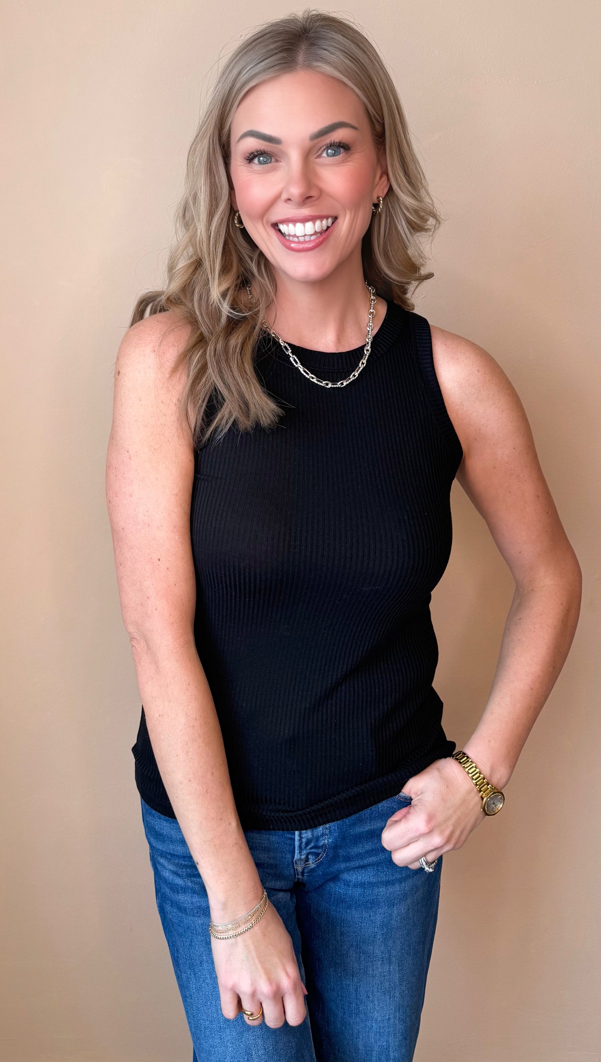 Woman wearing a black sleeveless top and blue jeans against a beige background