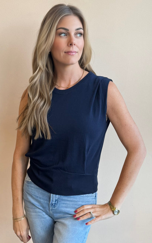 Woman wearing a navy sleeveless vest top and light blue jeans against a beige background