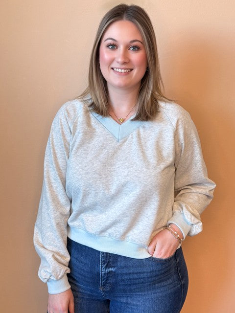 Woman wearing a light gray sweater and blue jeans against a beige background