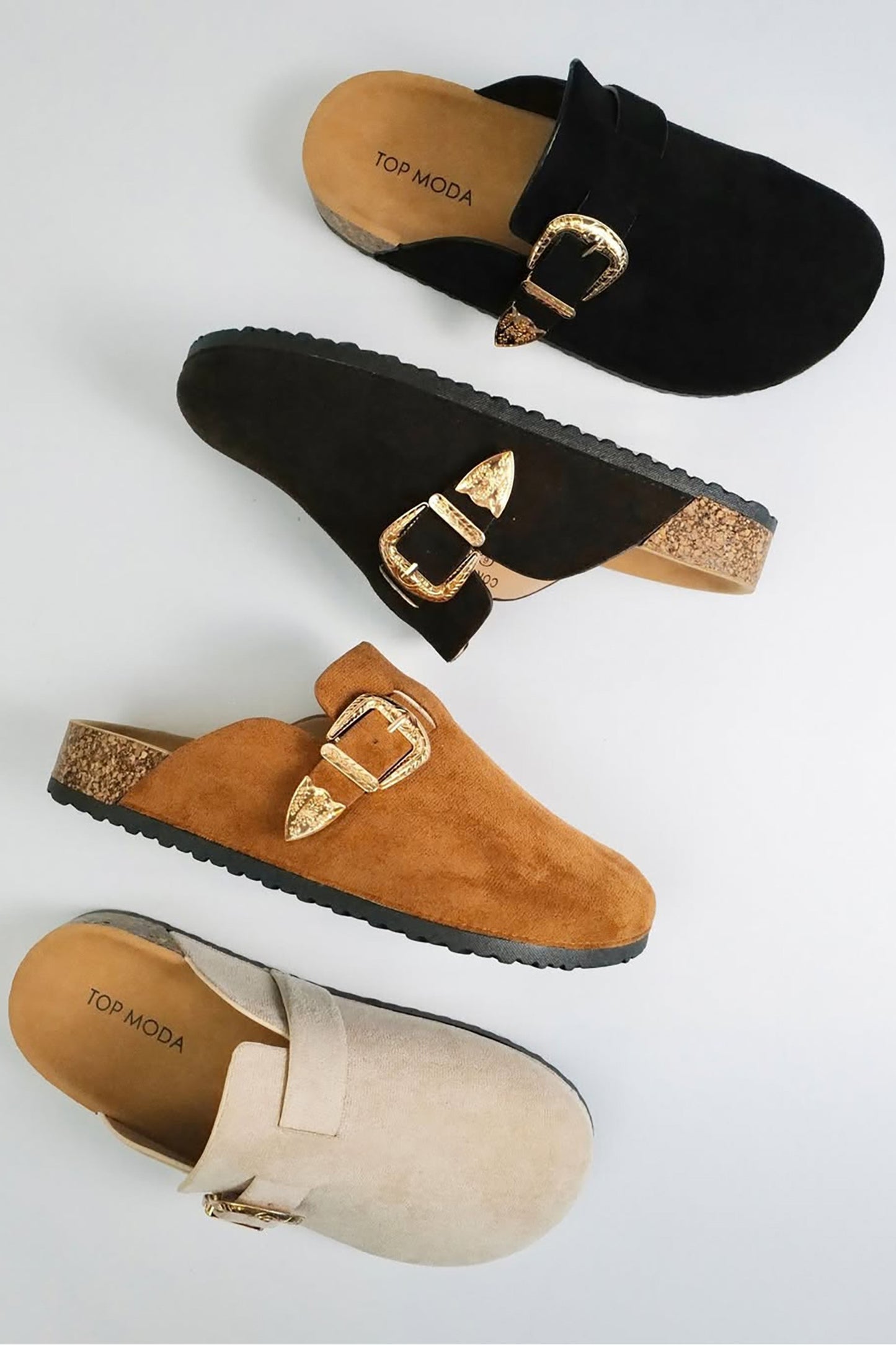 Black, brown, and beige suede clogs with gold buckles on a light gray background