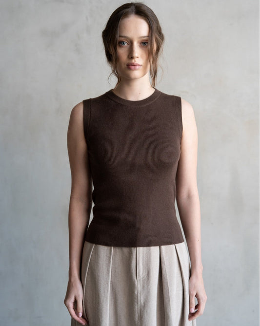 Woman wearing a brown sleeveless top and beige pants against a gray background