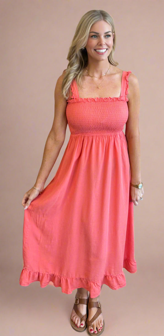 Woman wearing a coral dress standing against a beige wall.