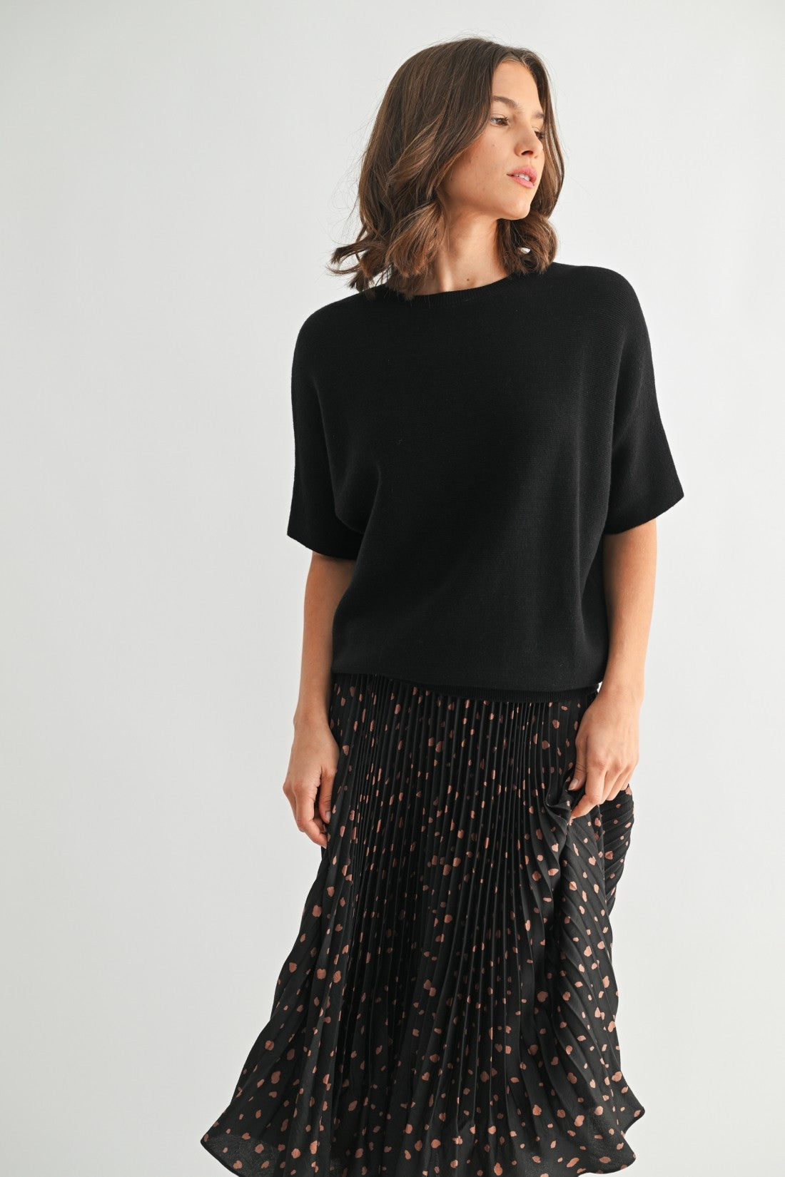 Woman wearing a black dolman top and black patterned skirt on a white background