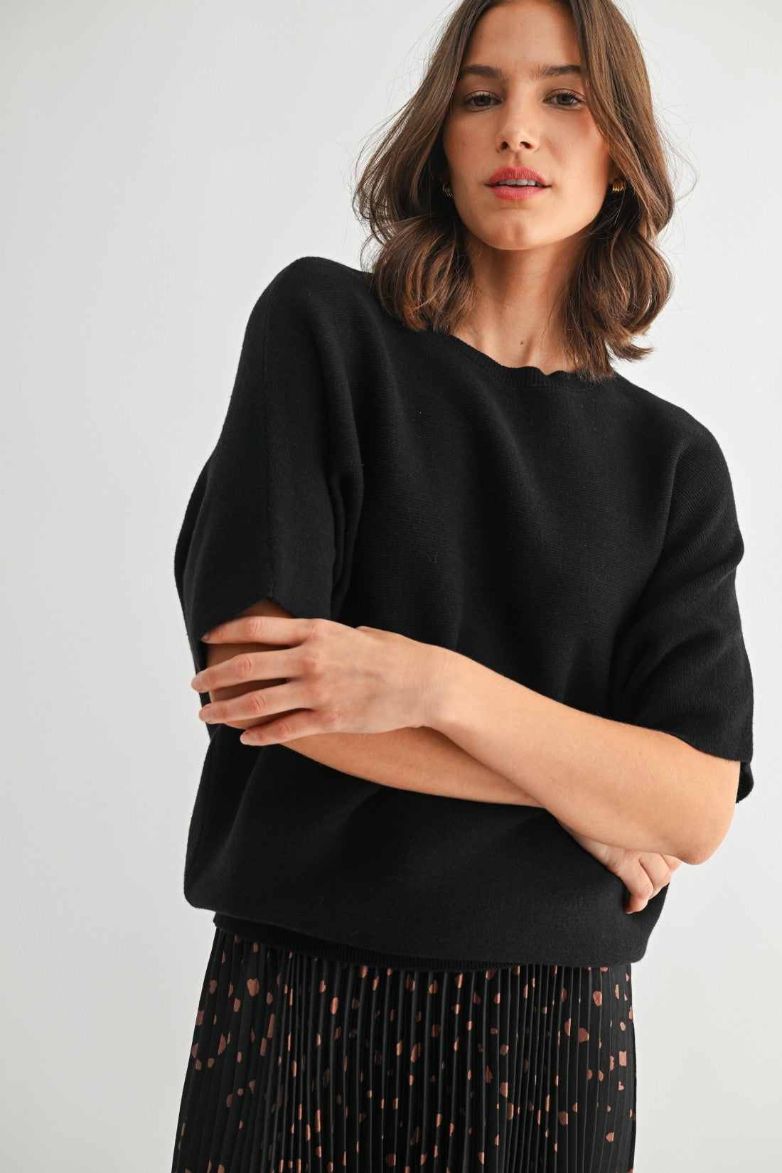 Woman wearing a black dolman sleeve top with a plain background