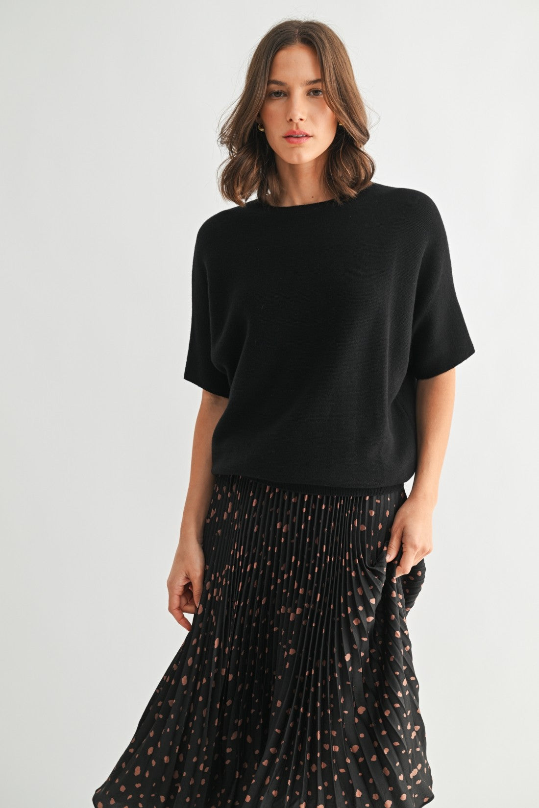 Woman wearing a black dolman sleeve top and patterned skirt on a white background