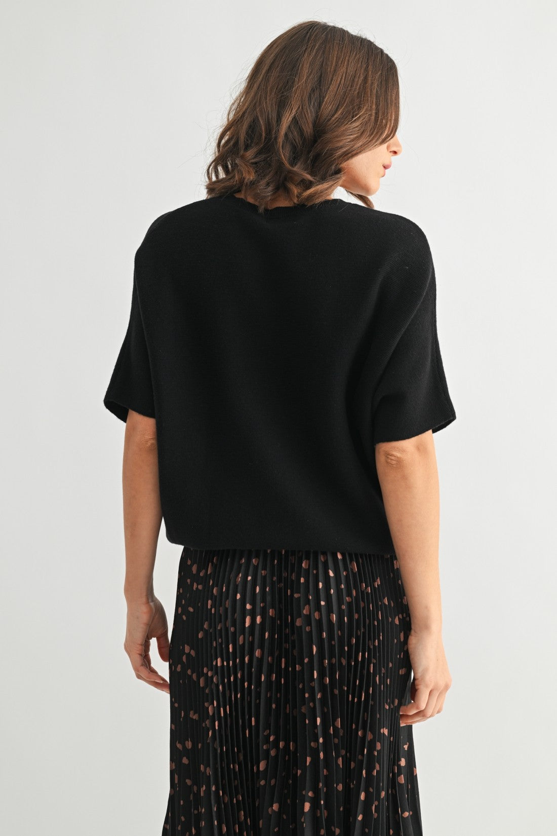 Woman wearing a black dolman sleeve short-sleeve top and patterned skirt on a white background