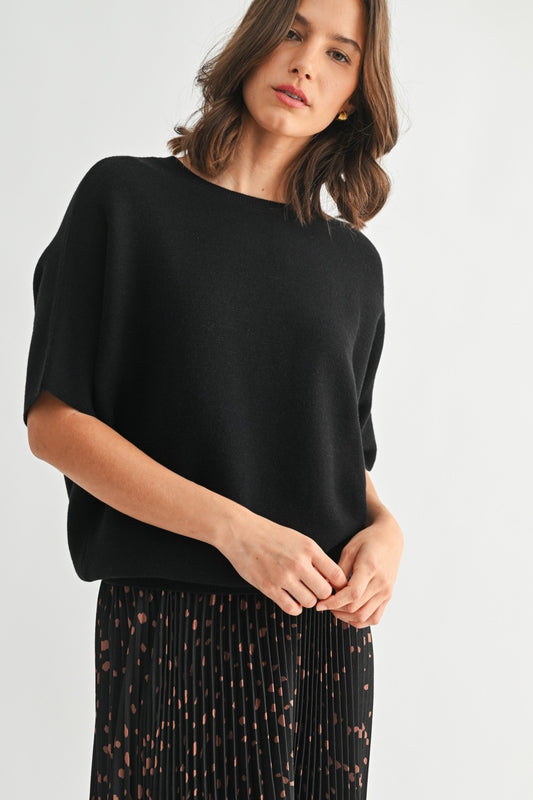 Woman wearing a black dolman top and patterned skirt on a white background