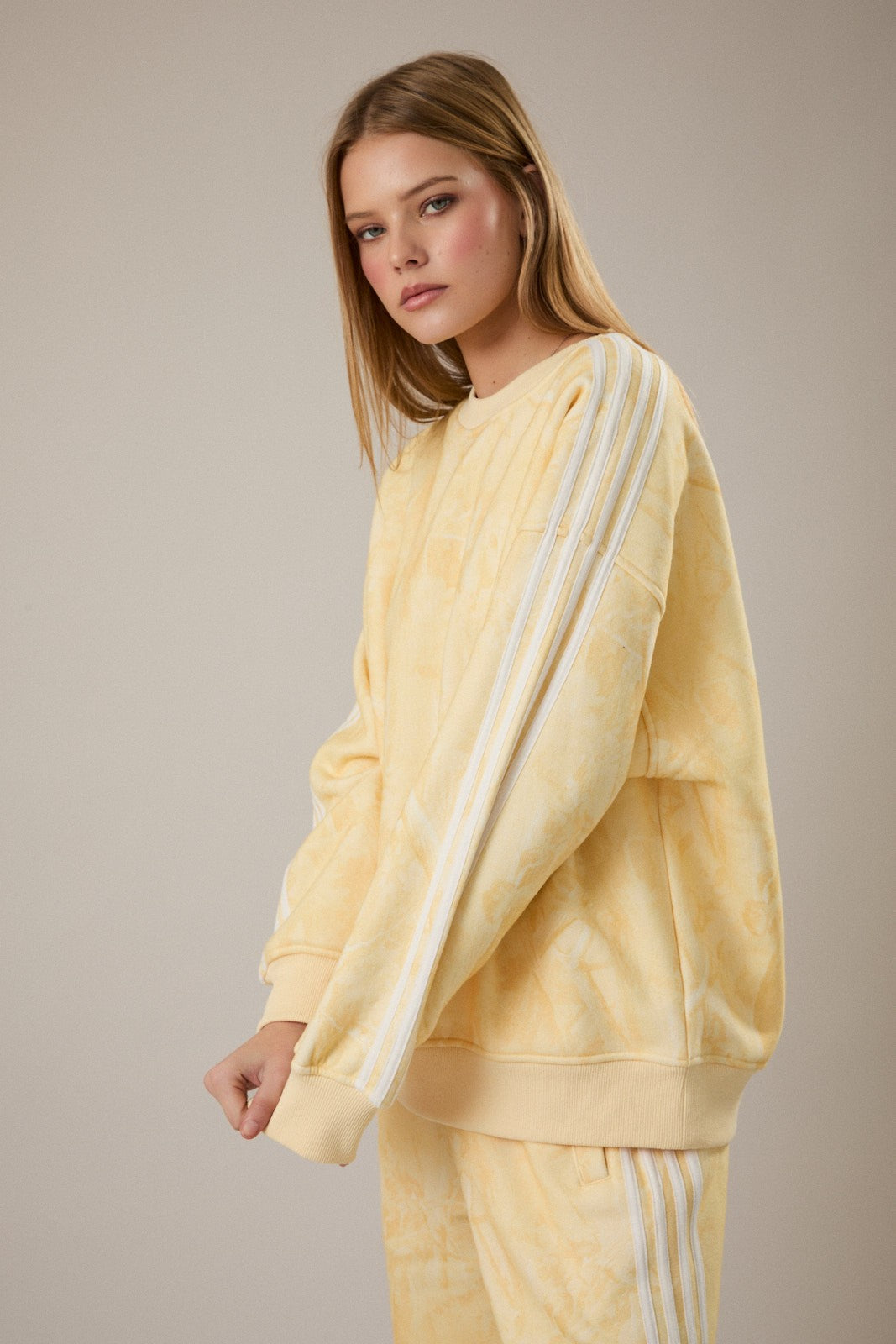 Woman wearing a yellow tie-dye Adidas tracksuit against a beige background