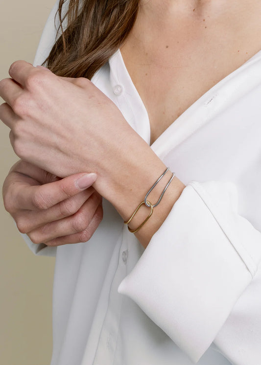Person wearing a white shirt with a mixed-metal bracelet on a neutral background