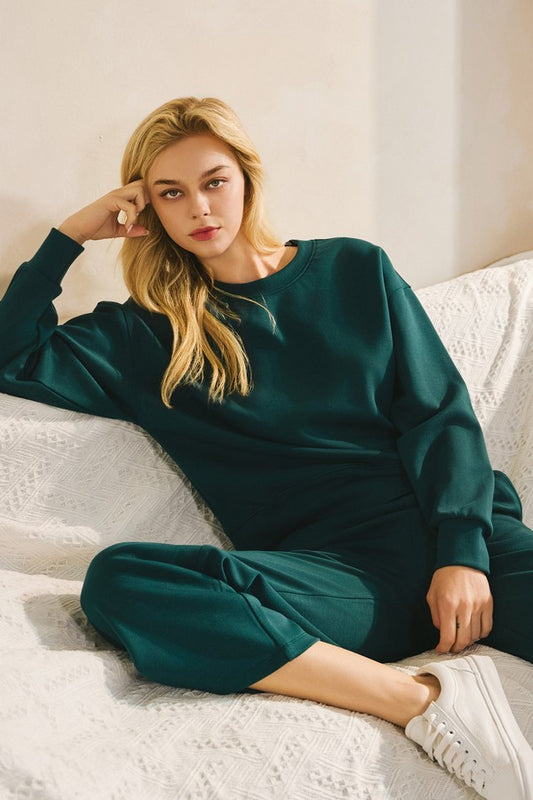 Woman wearing a green tracksuit sitting on a white couch.
