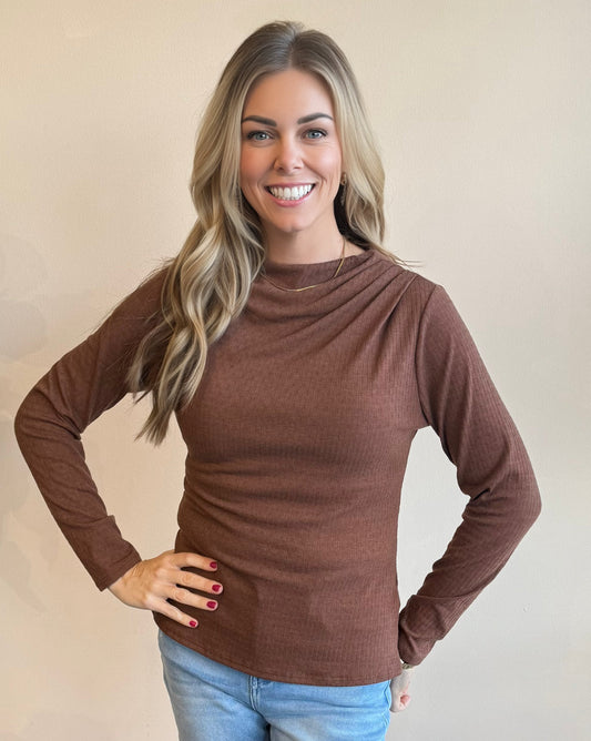Woman wearing a chocolate brown long-sleeve top against a beige background