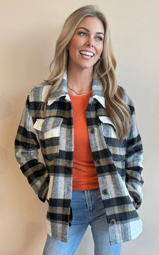 Woman wearing a black plaid shacket over an orange top with a beige background