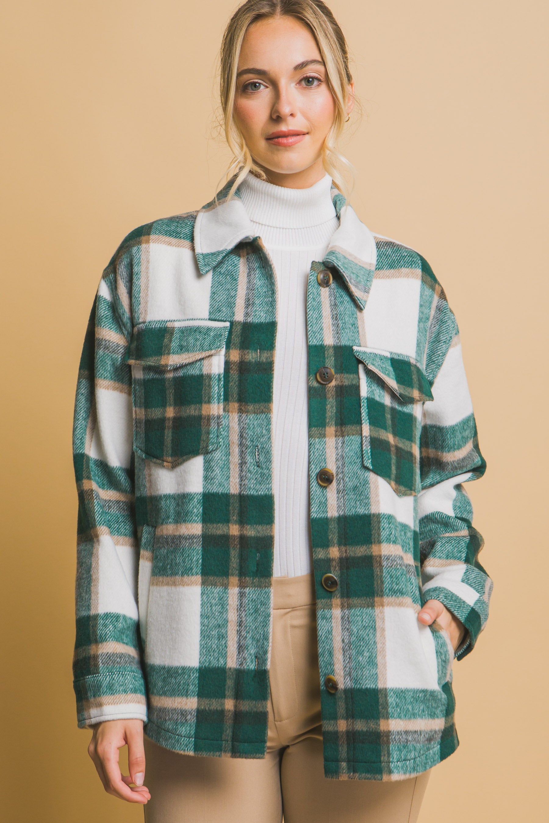 Woman wearing a green and white plaid shacket over a white turtleneck on a beige background