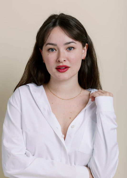Woman wearing a white shirt with simple gold necklace against a beige background