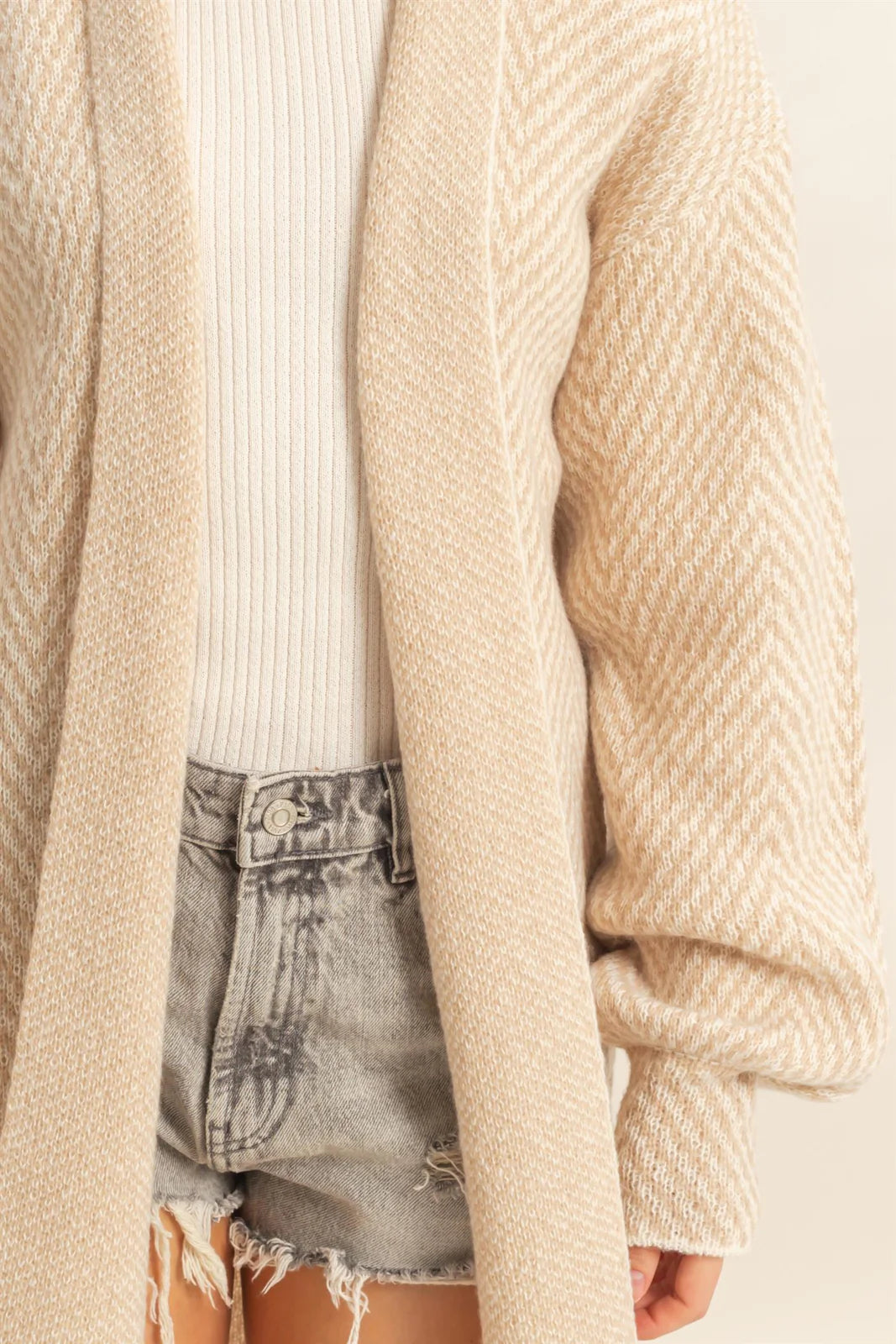 Beige cardigan over a white shirt and denim shorts on a neutral background