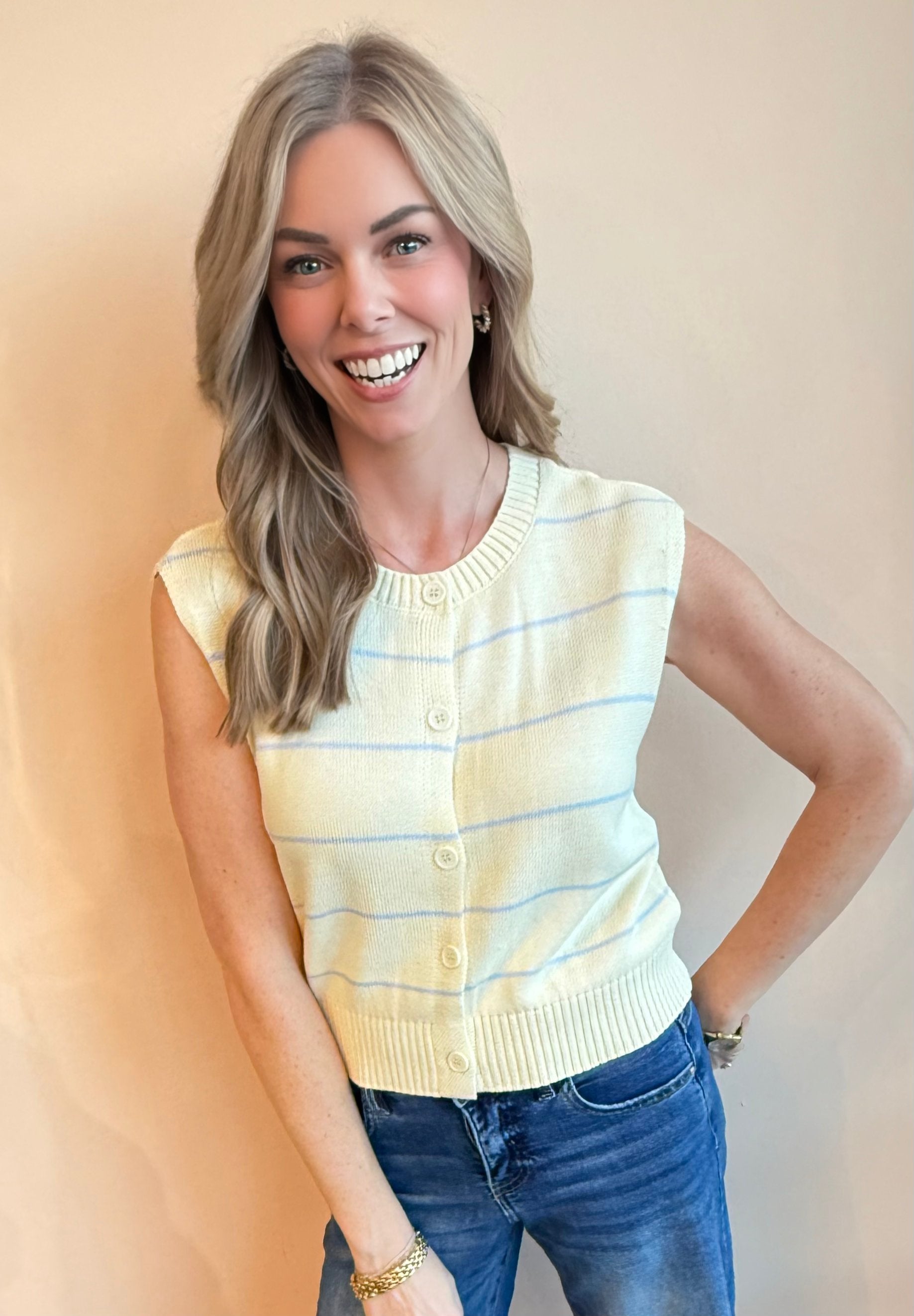 Woman wearing a yellow striped sleeveless sweater and blue jeans against a beige background