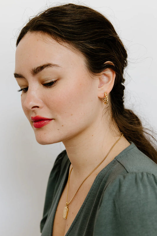 Woman wearing gold earrings and necklace against a white background