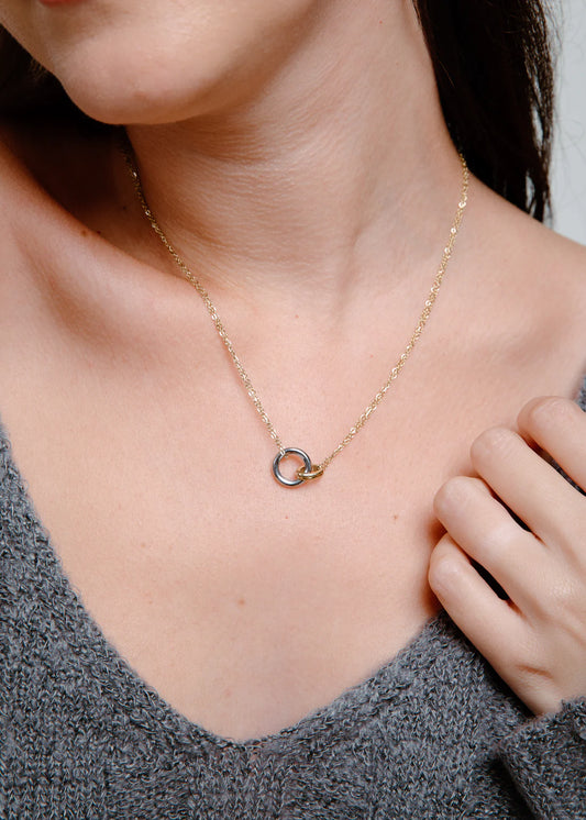 Close-up of a person wearing a delicate mixed-metal necklace with a small hooked circles pendant.