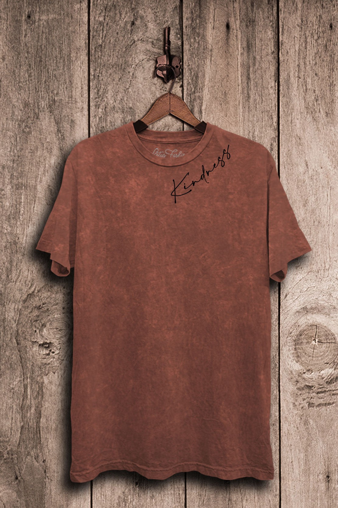 Brown t-shirt with 'Kindness' text on a wooden background