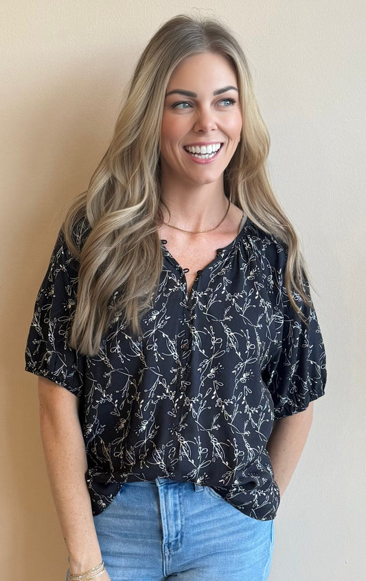 Woman wearing a black floral patterned blouse and blue jeans against a beige background