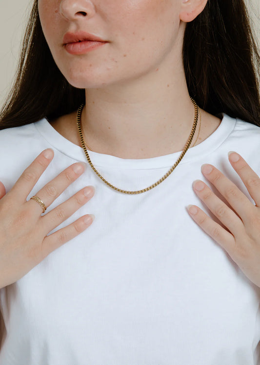 Person wearing a gold necklace wearing a plain white t-shirt