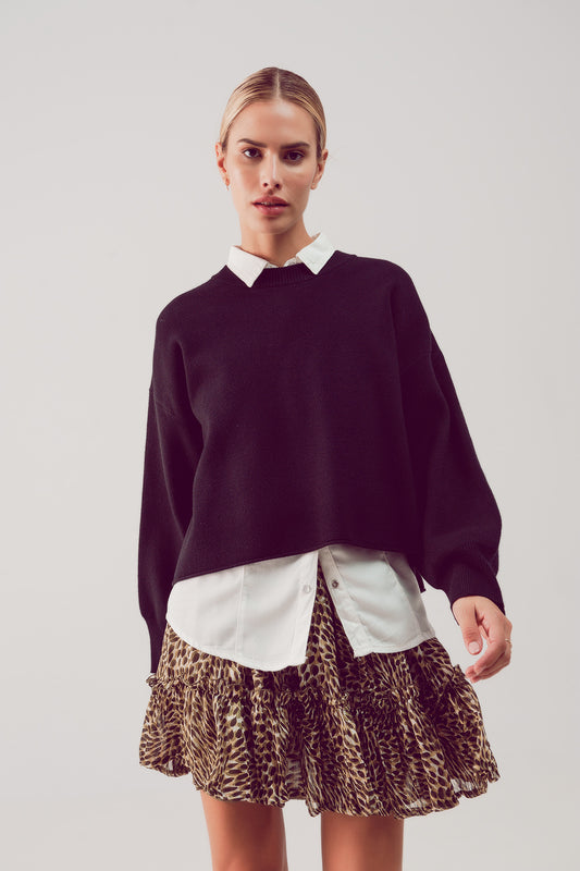 Woman wearing a dark black sweater over a white shirt with a leopard print skirt on a plain background