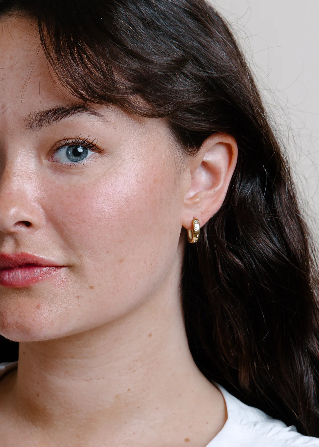 Close-up of a woman wearing gold hoop earrings with a neutral background