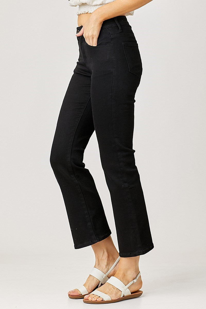 Person wearing black risen jeans and white sandals on a plain background