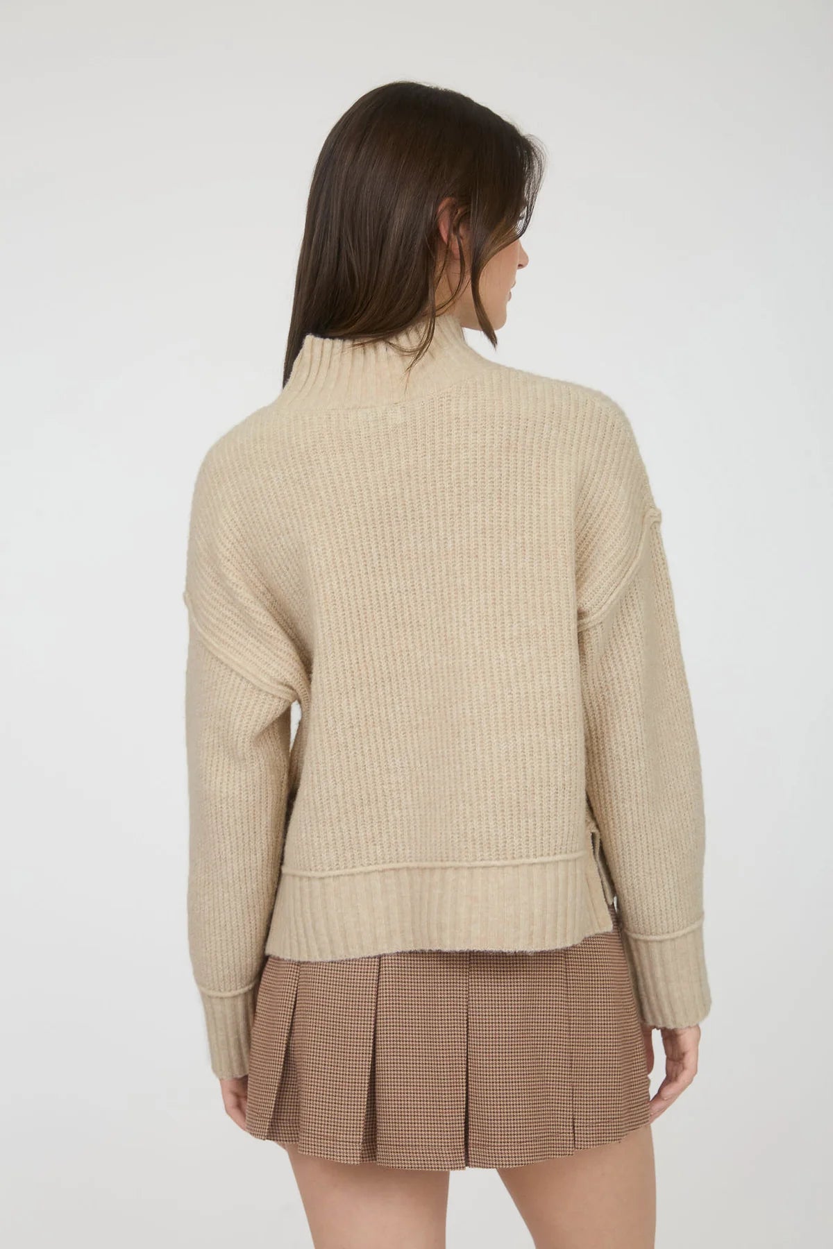Woman wearing a beige ribbed sweater and plaid skirt on a white background