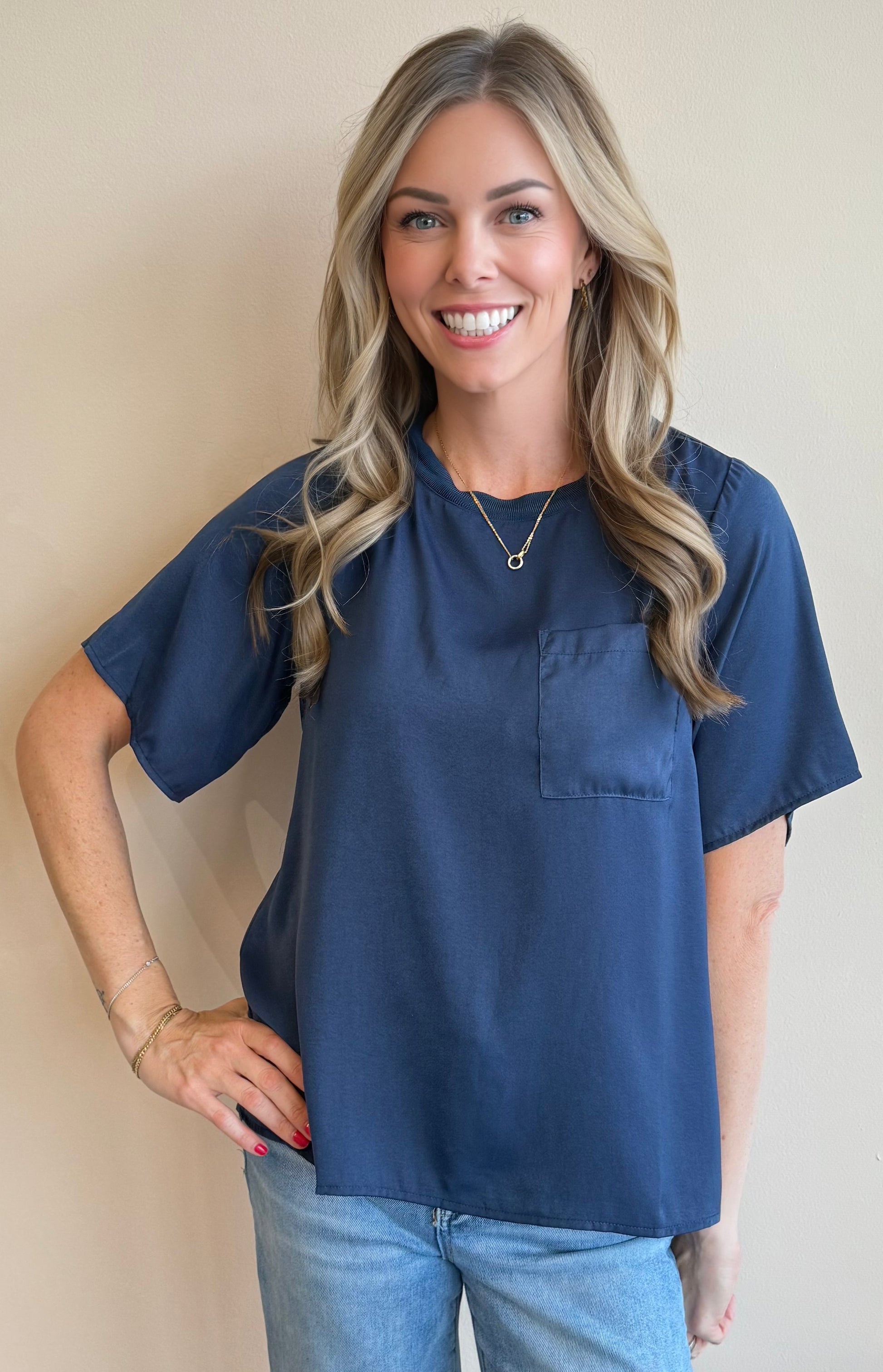 Woman wearing a navy blue top with a pocket against a beige wall