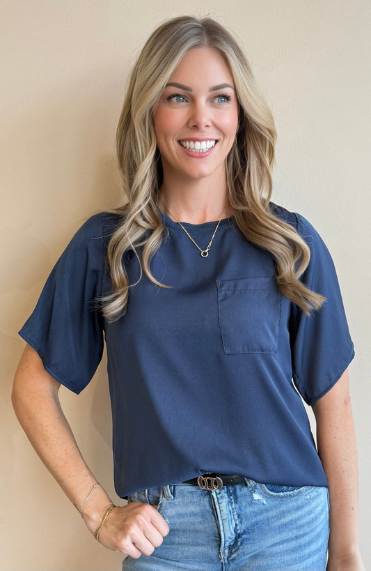 Woman wearing a navy top and jeans against a beige background