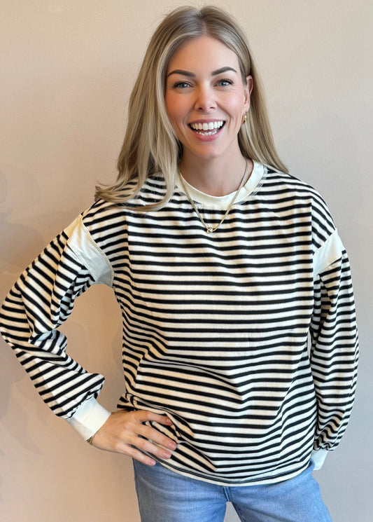 Woman wearing a black and white striped long-sleeve top with a plain background