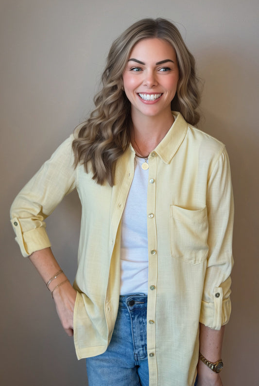 Woman wearing a light yellow shirt over a white top and blue jeans, standing against a plain background.