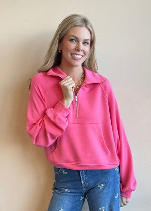 Woman wearing a pink pullover and blue jeans against a beige wall.