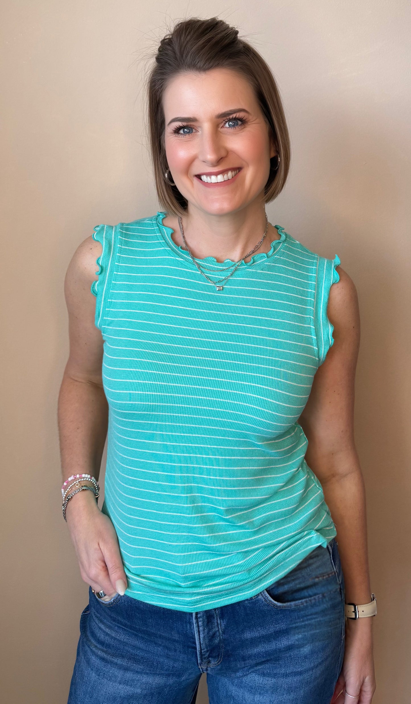 Woman wearing a teal striped sleeveless top and blue jeans against a beige background