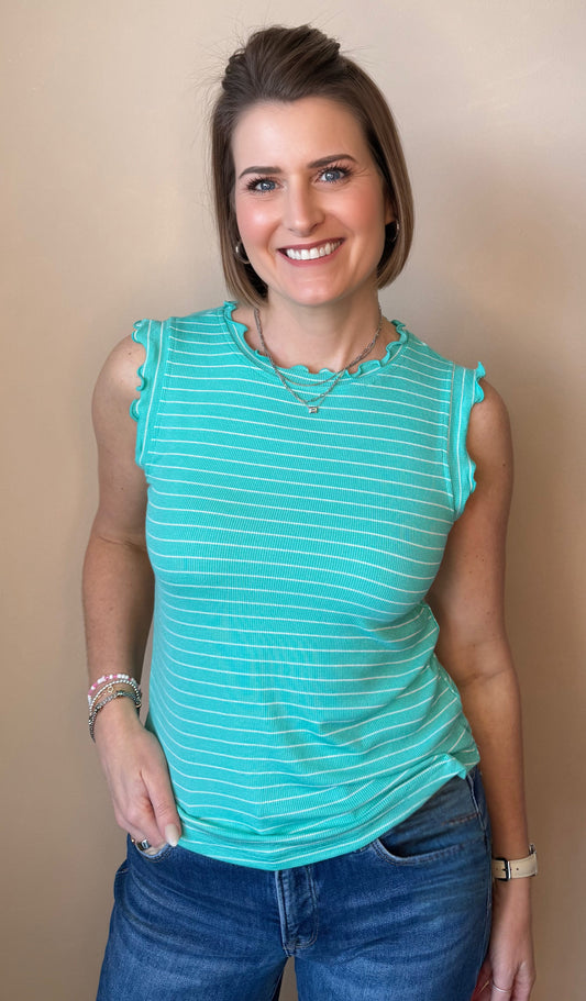 Woman wearing a teal striped sleeveless top and blue jeans against a beige background