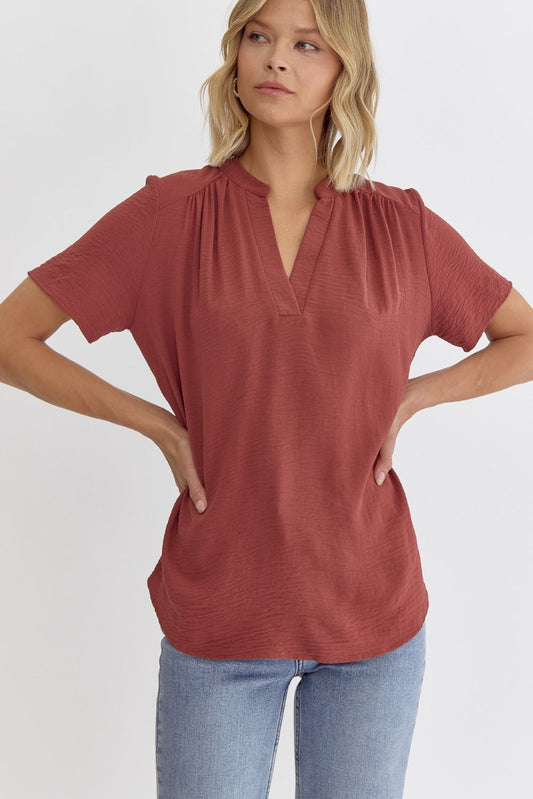 Woman wearing a rust-colored short-sleeve top and light blue jeans on a white background