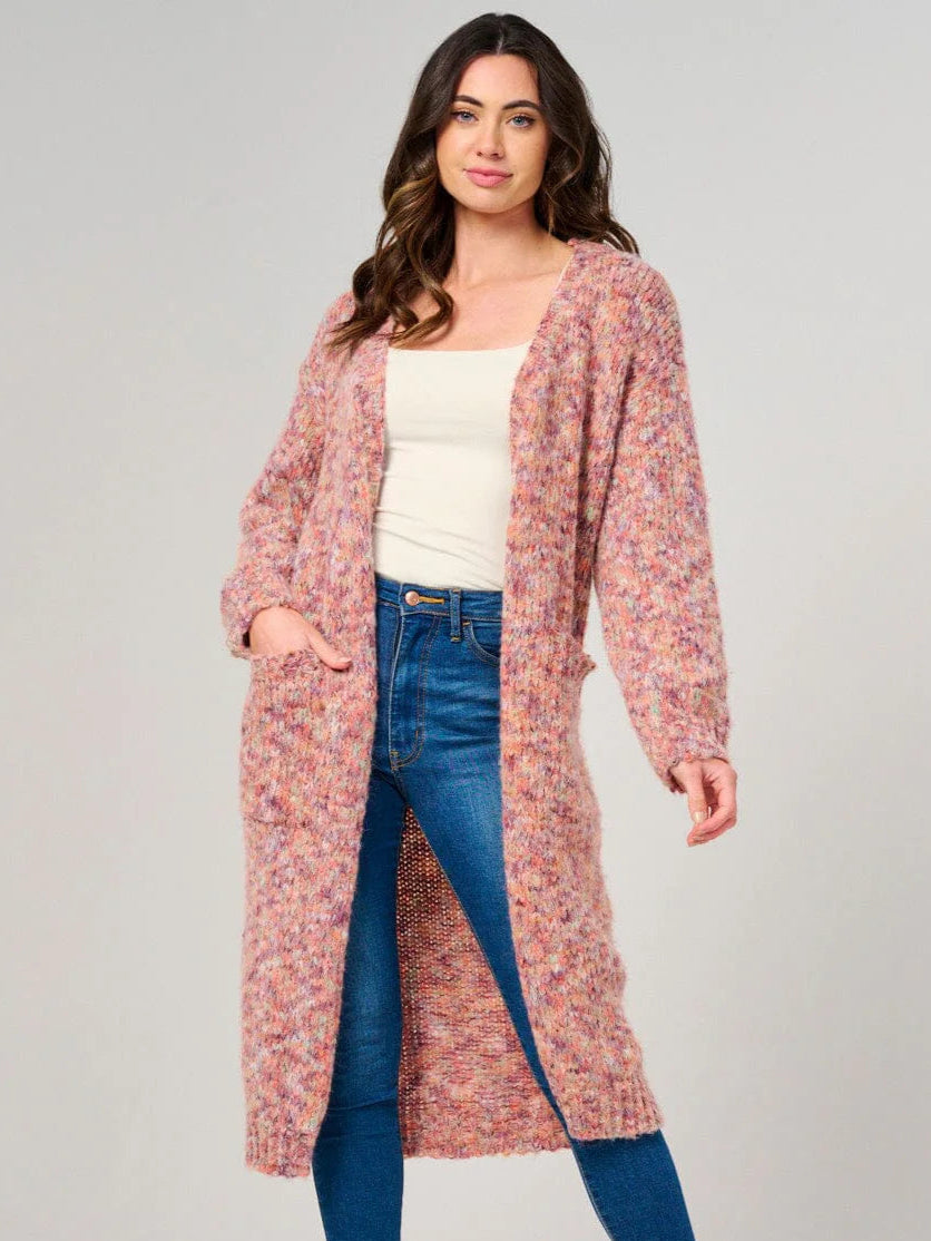 Woman wearing a long pink cardigan, white top, and blue jeans on a gray background
