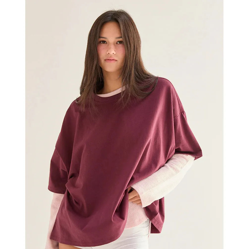 Woman wearing a burgundy oversized sweater over a white shirt on a plain background