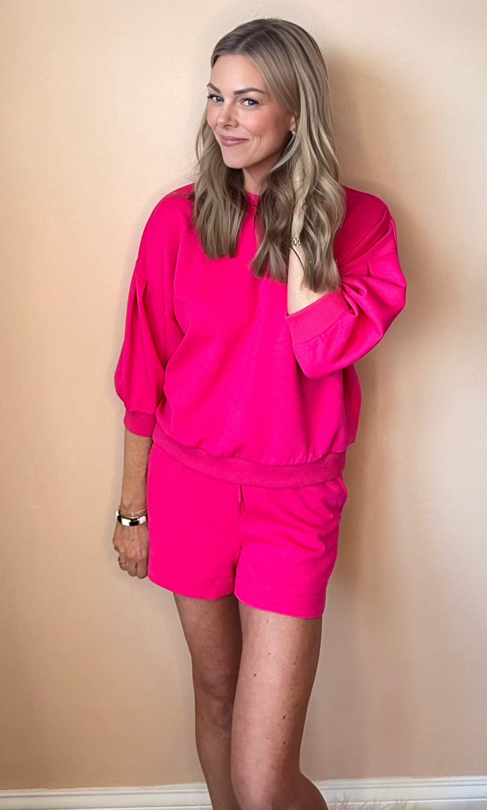 Woman wearing a bright pink outfit against a beige wall